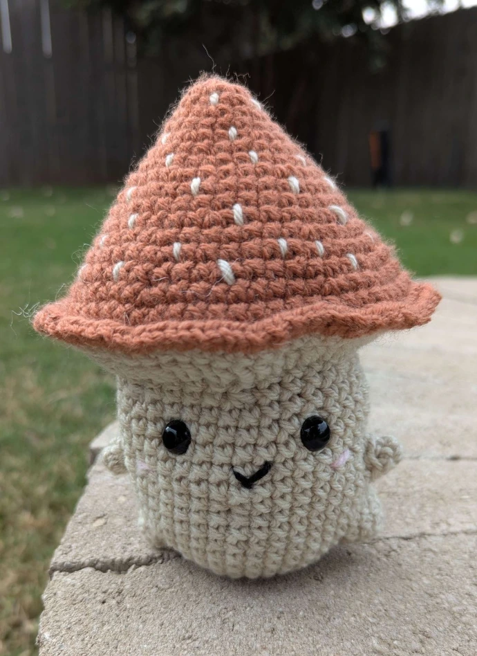 Crocheted mushroom with a orangebrown top and a smiling face