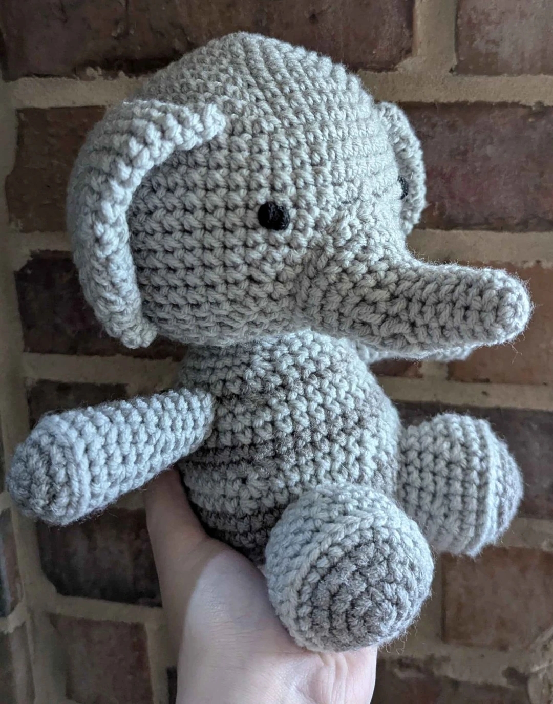 Crocheted elephant facing to the right held up by a hand